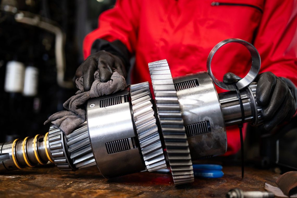 Gloved hands inspect a metal gear shaft on a workbench in a workshop.