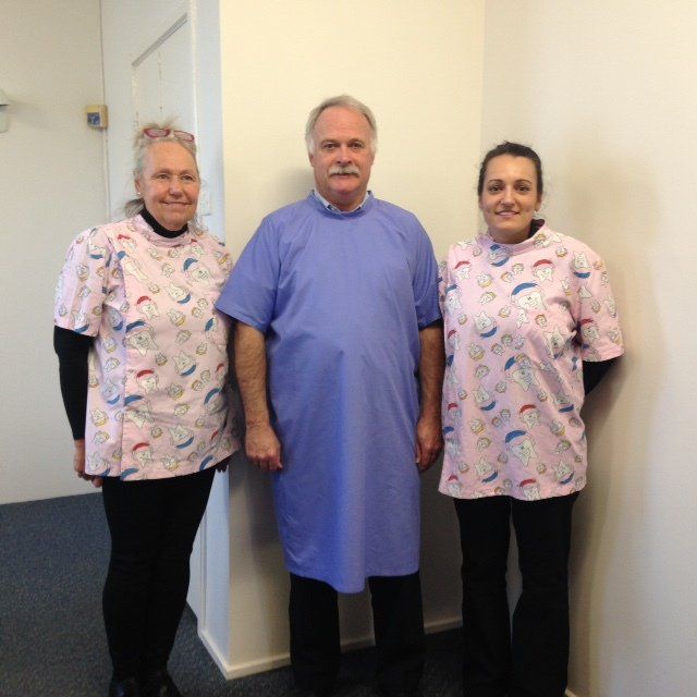 Three healthcare staff stand in a hallway wearing pink patterned scrubs and a blue gown