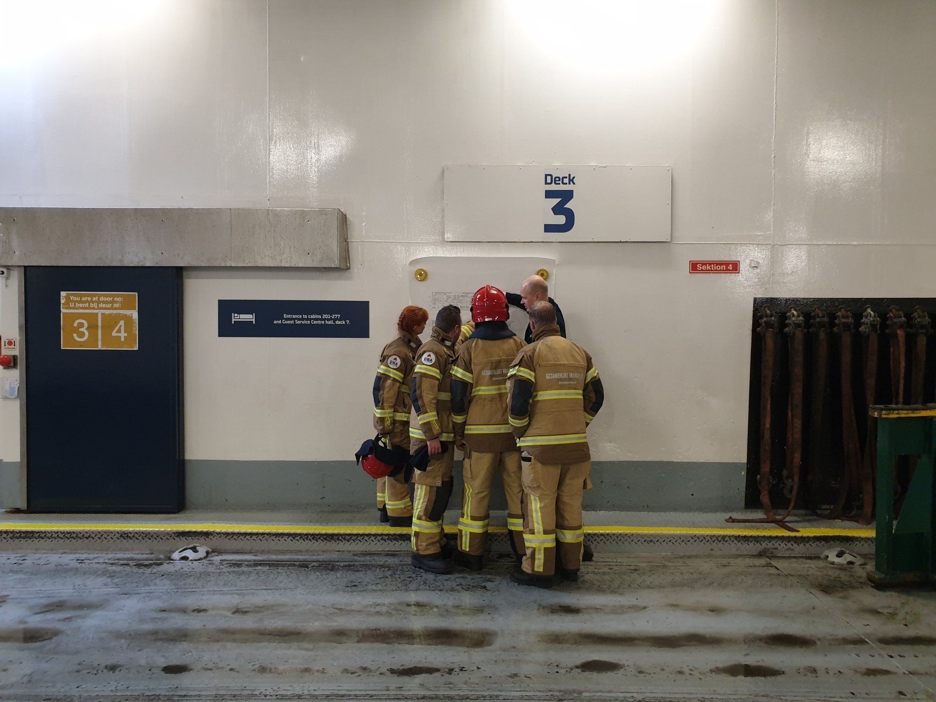 Brandweerlieden in beschermende kleding inspecteren een muur met het opschrift 