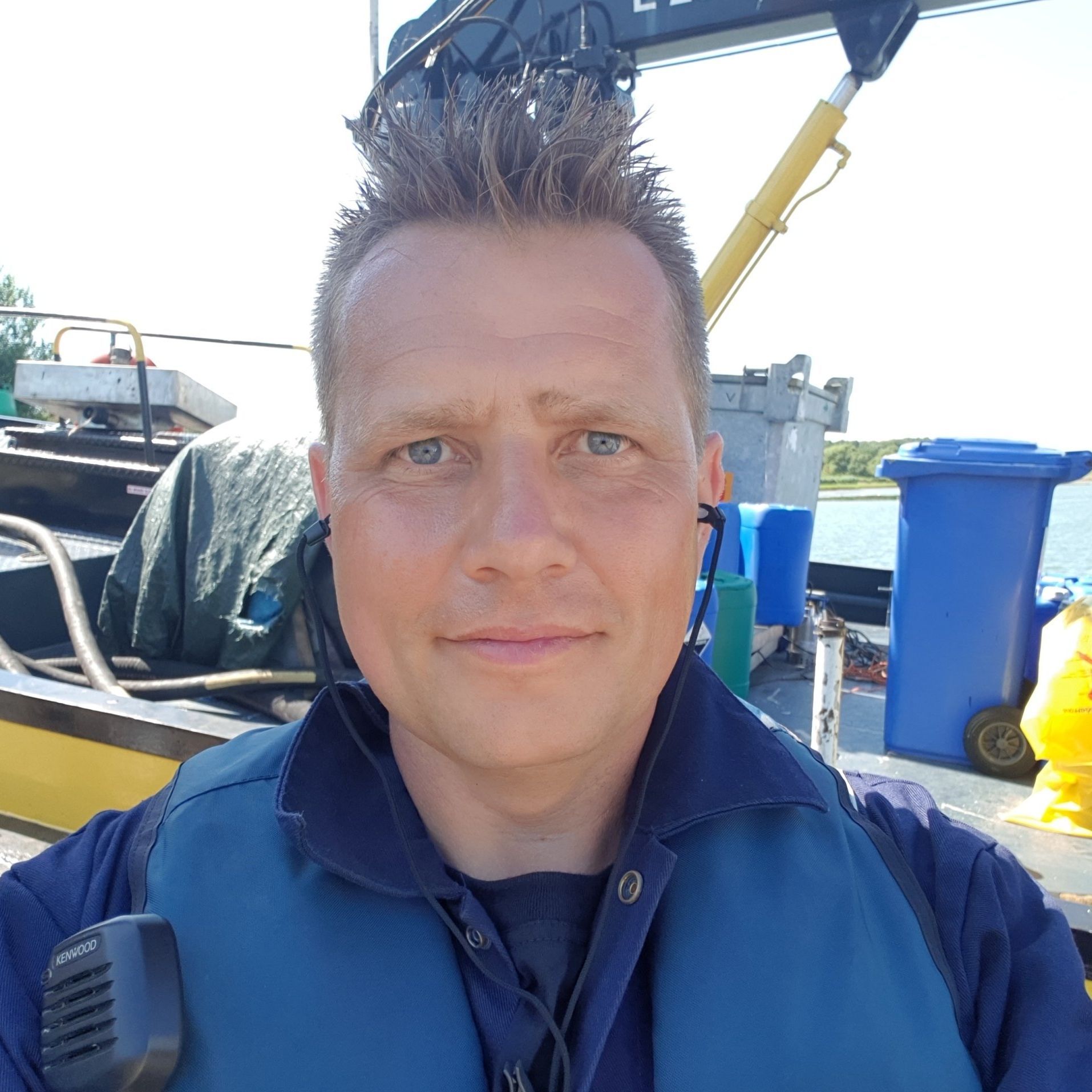 Man met een blauw veiligheidsvest staat op een boot vlak bij het water.