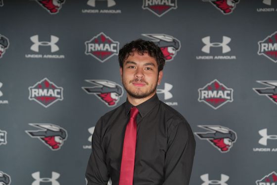 Kai Vong in black shirt and red tie posing before RMAC and Under Armour backdrop