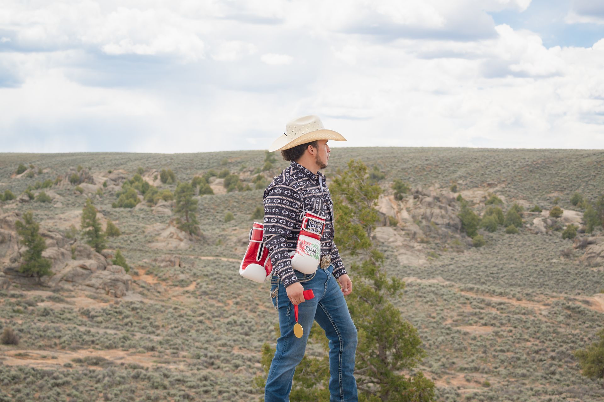 Person in cowboy hat standing in a desert landscape with a red backpack and water bottle