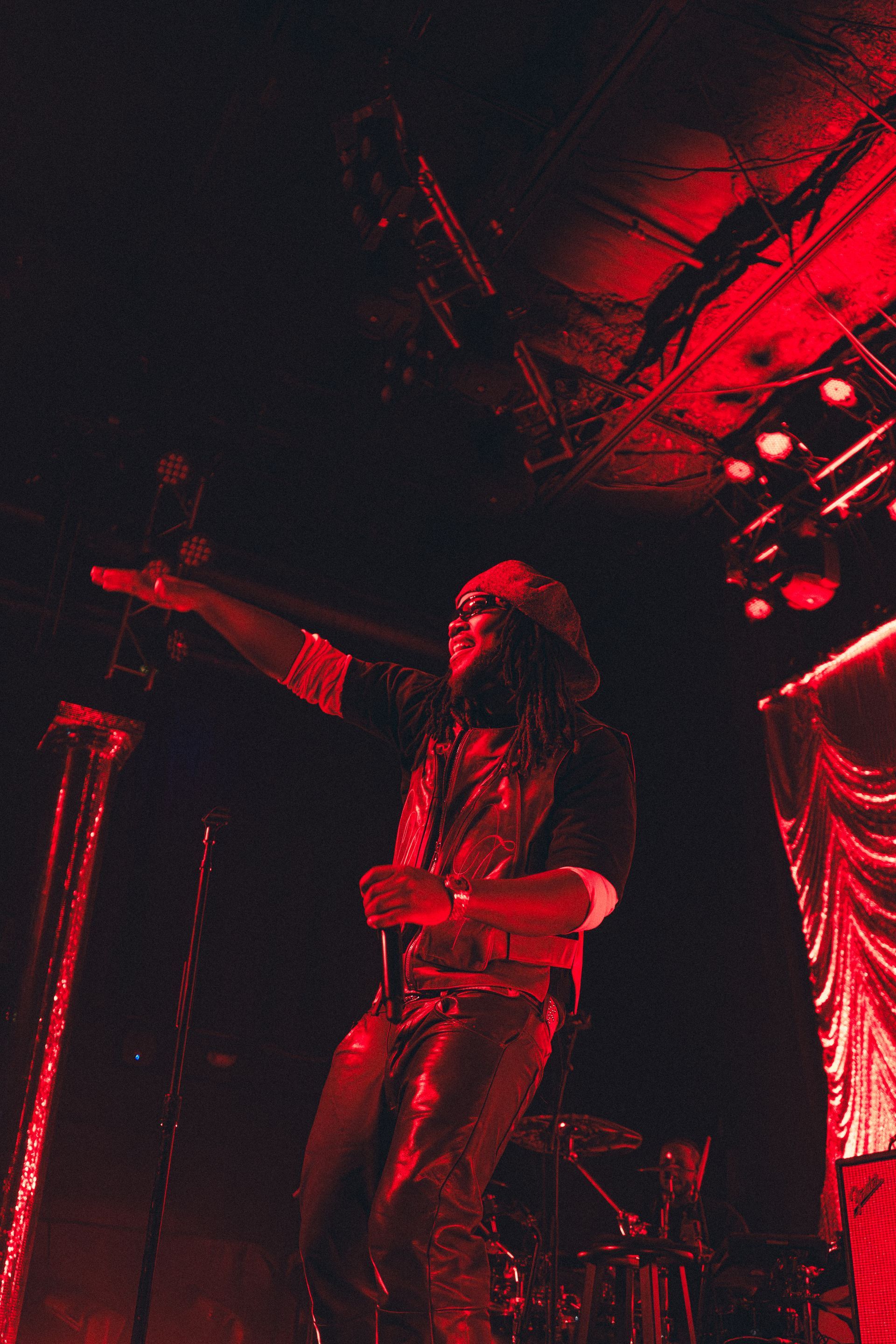 Leon Thomas performing onstage under red lighting, pointing toward the audience.
