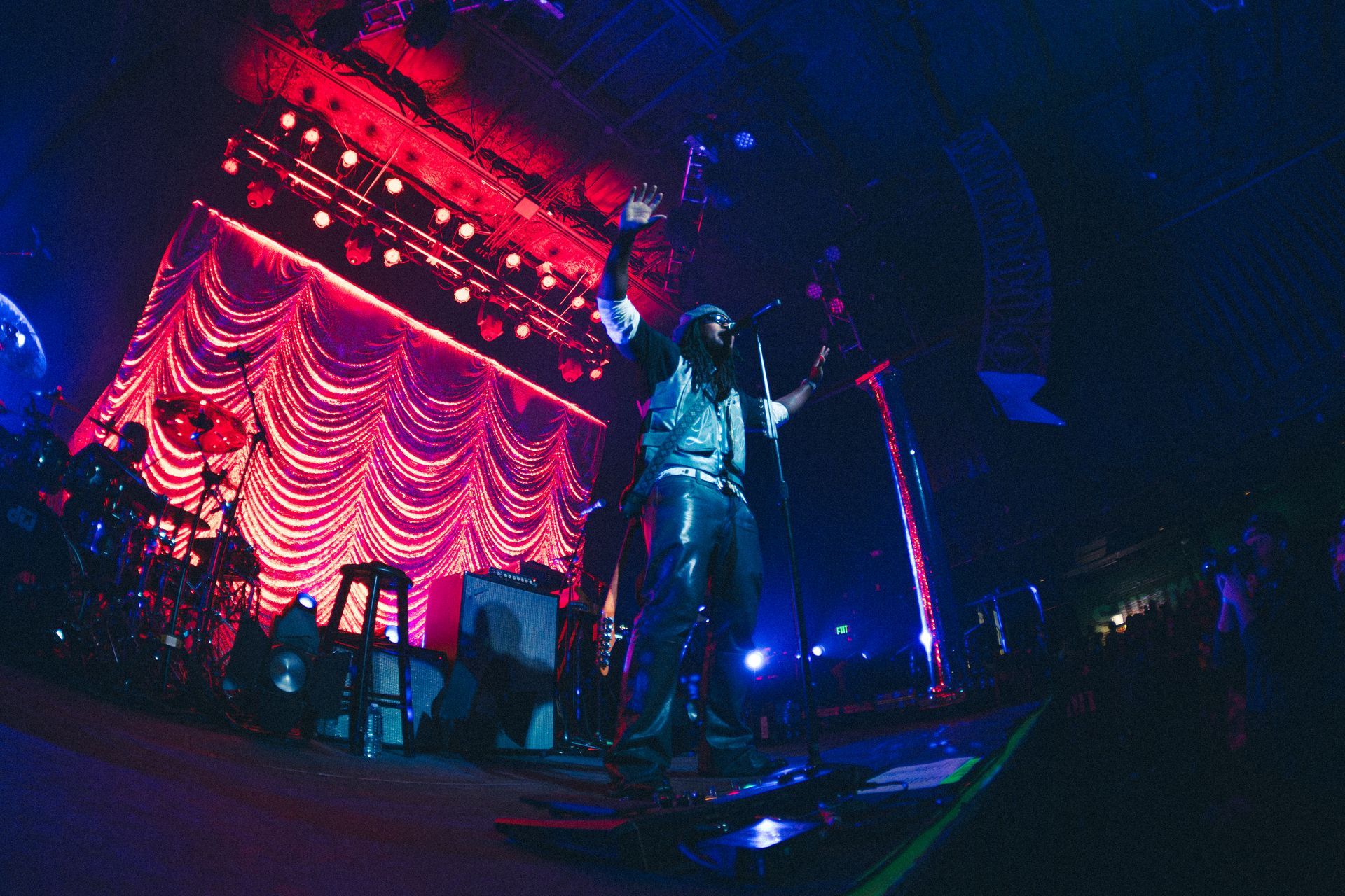 Leon Thomas on stage under red and blue lights, performing before a draped backdrop in a dark concert venue