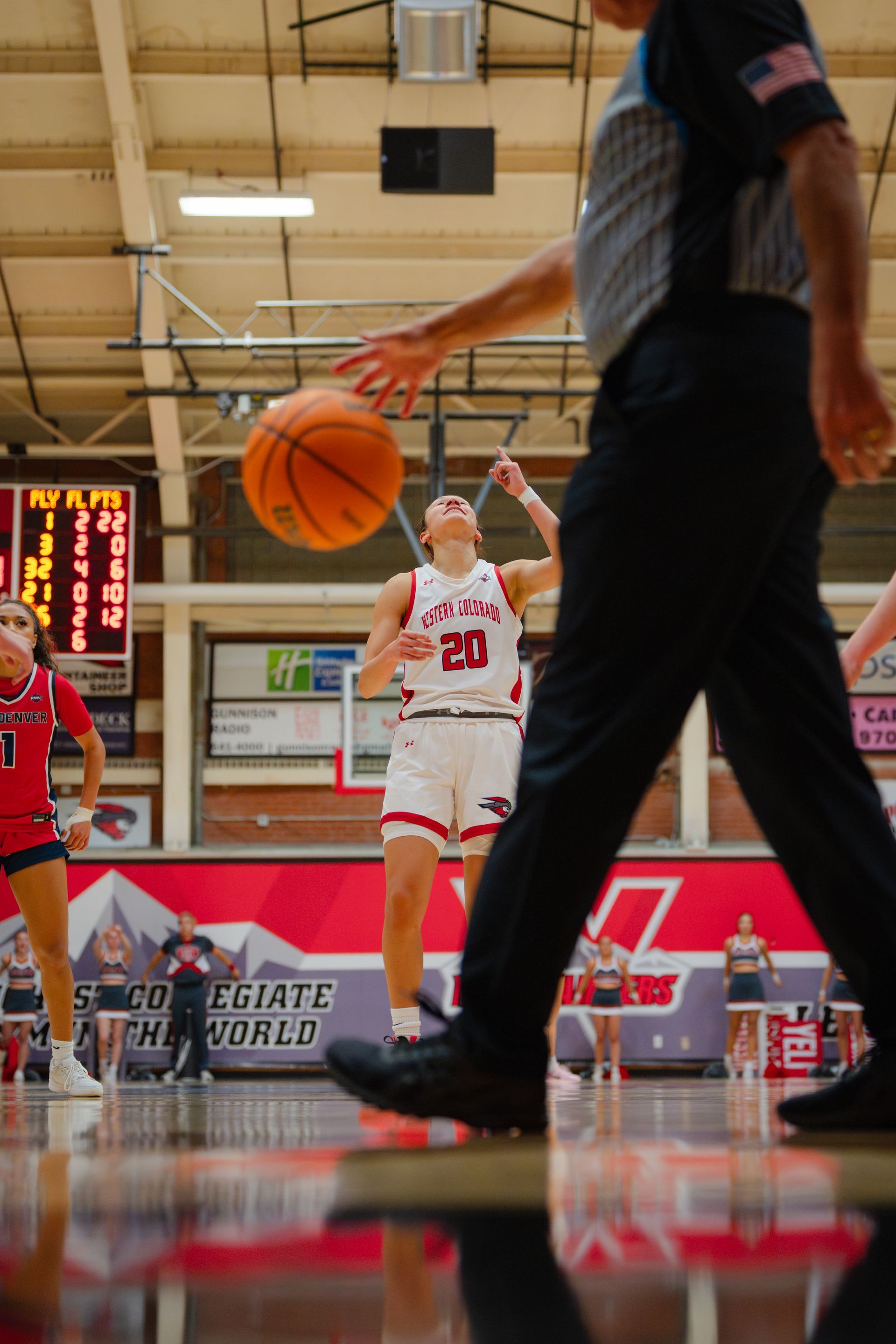 Basketball player in white jersey dribbles on court as referee passes in foreground