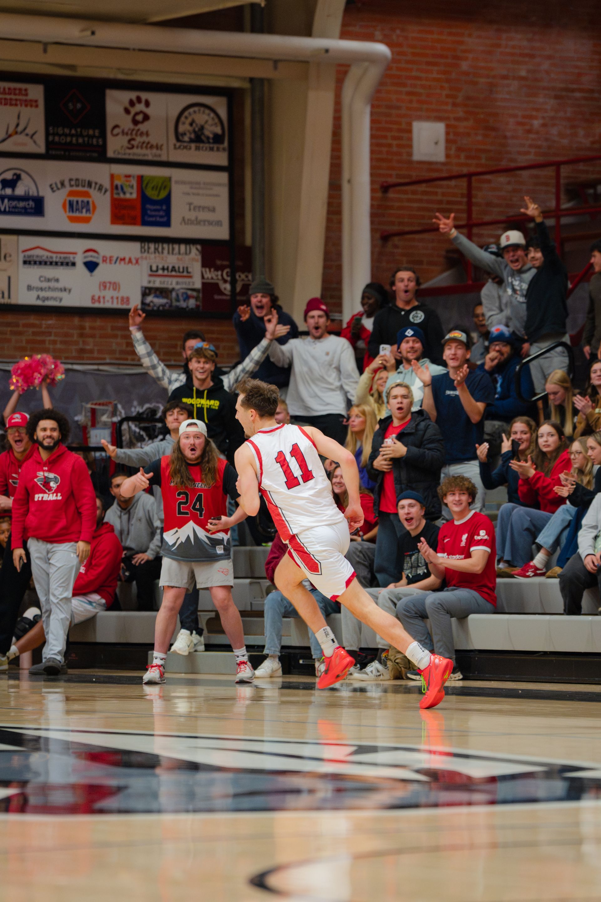 Aidan McDowell in white celebrates toward the hoop as fans cheer in the stands.