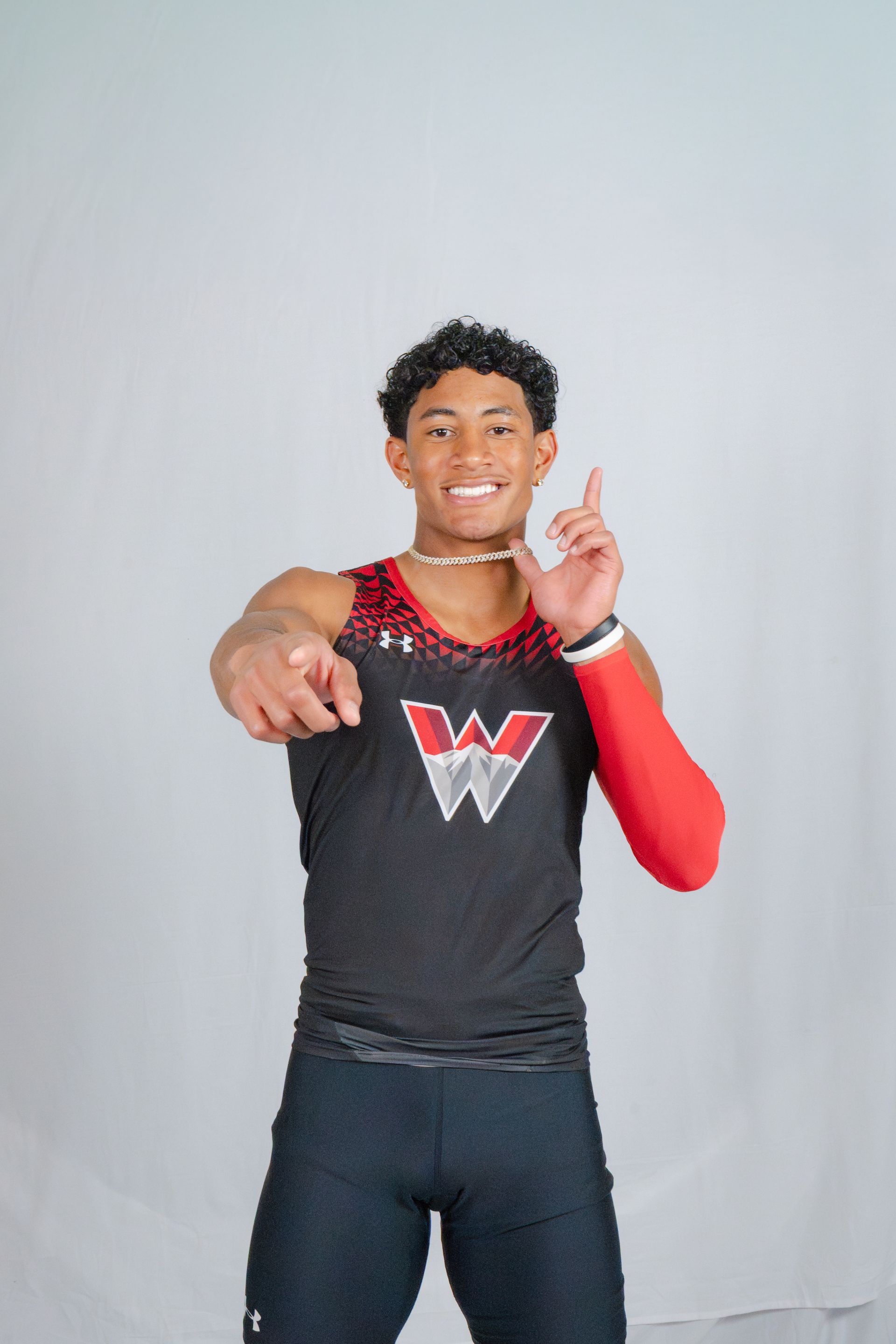 Smiling athlete in a black and red W logo jersey pointing at the camera against a gray backdrop