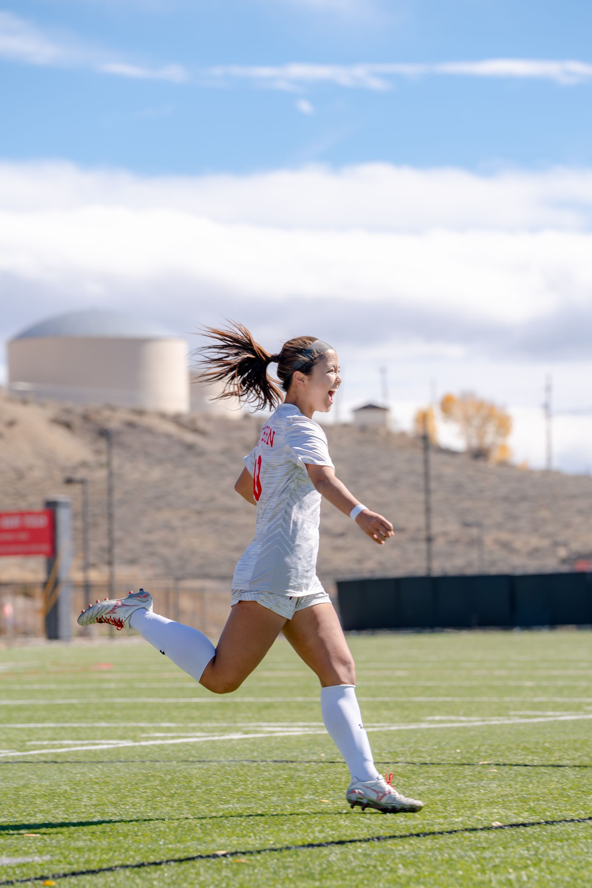 Soccer player in white uniform running on a field under a blue sky