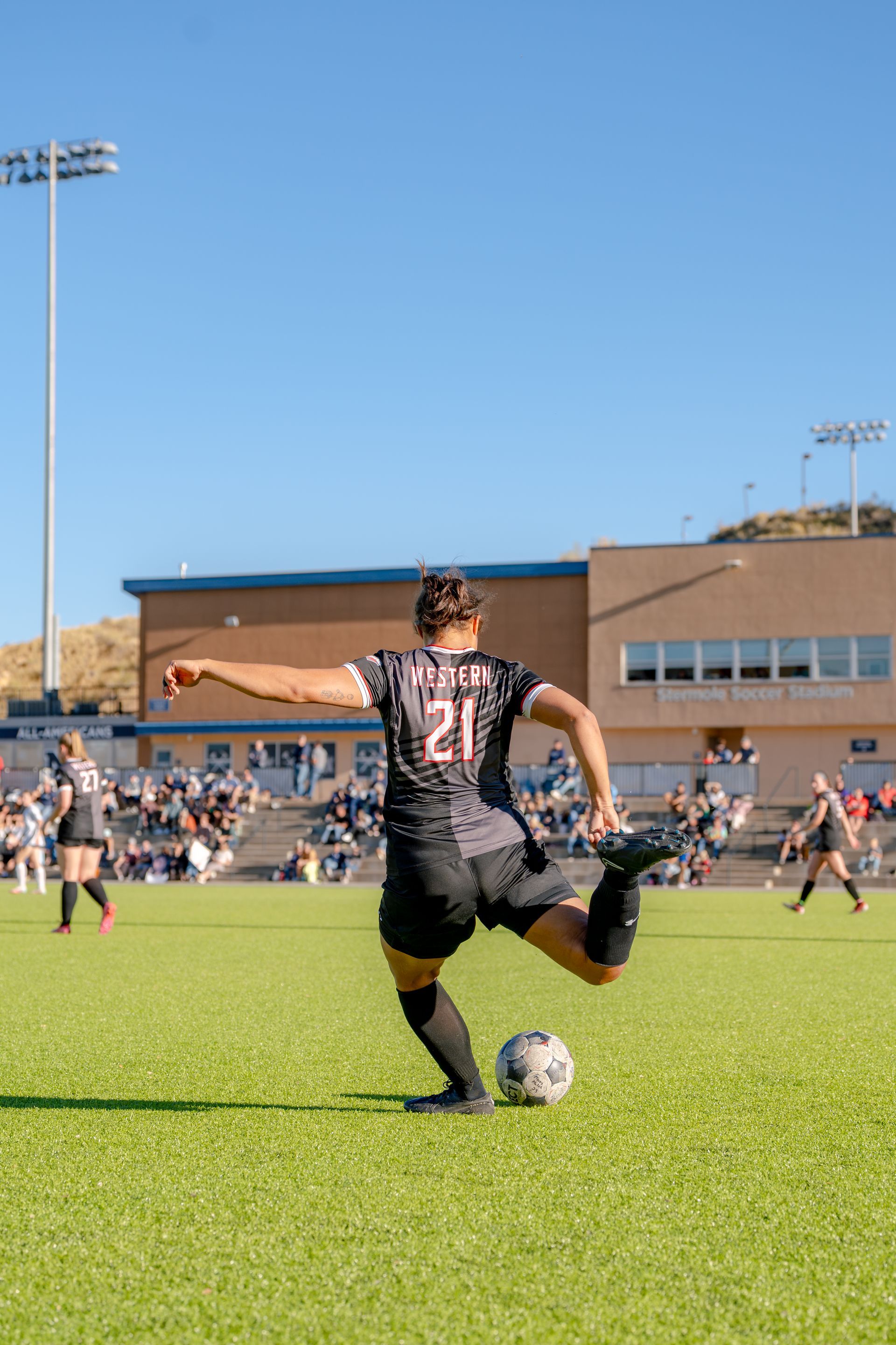 Soccer player in black jersey kicks ball on a sunny field during a match