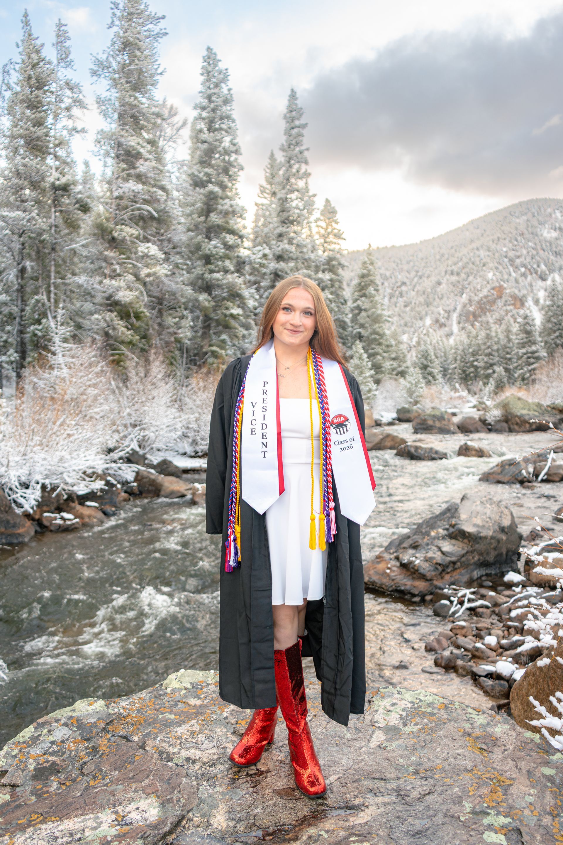 Person in a black coat and red boots standing by a snowy river in a winter mountain landscape