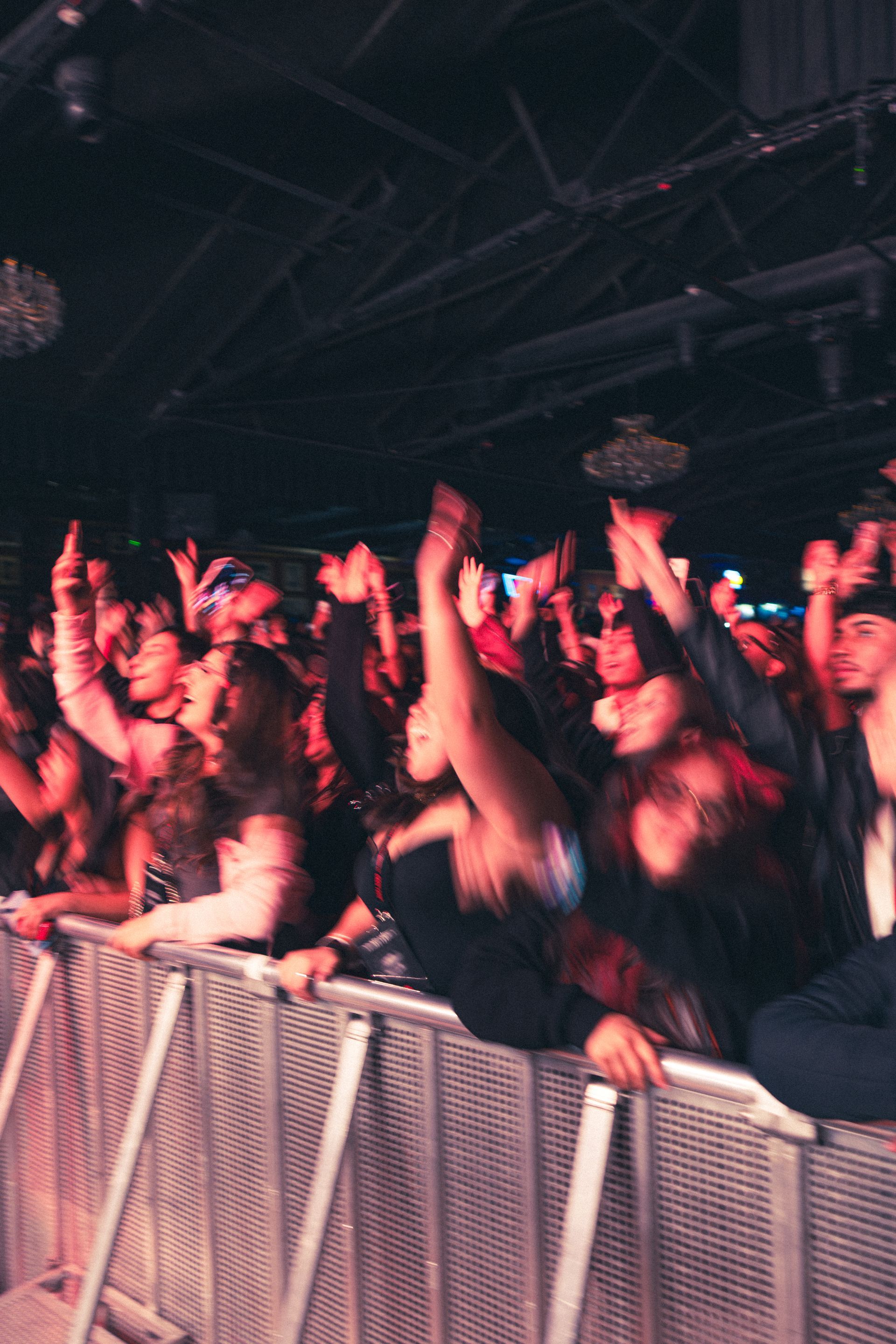 Crowd cheering with raised hands at a concert behind a metal barrier