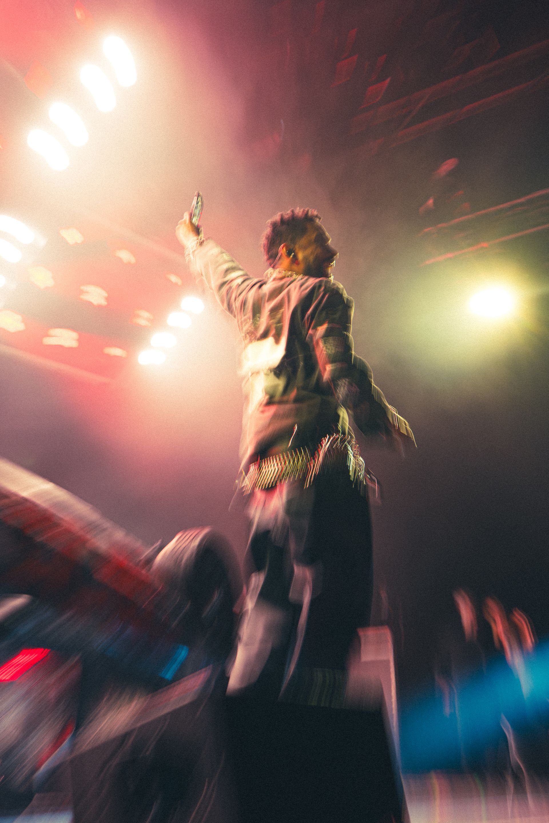 Miguel on a lit concert stage, arm raised under bright red and white lights