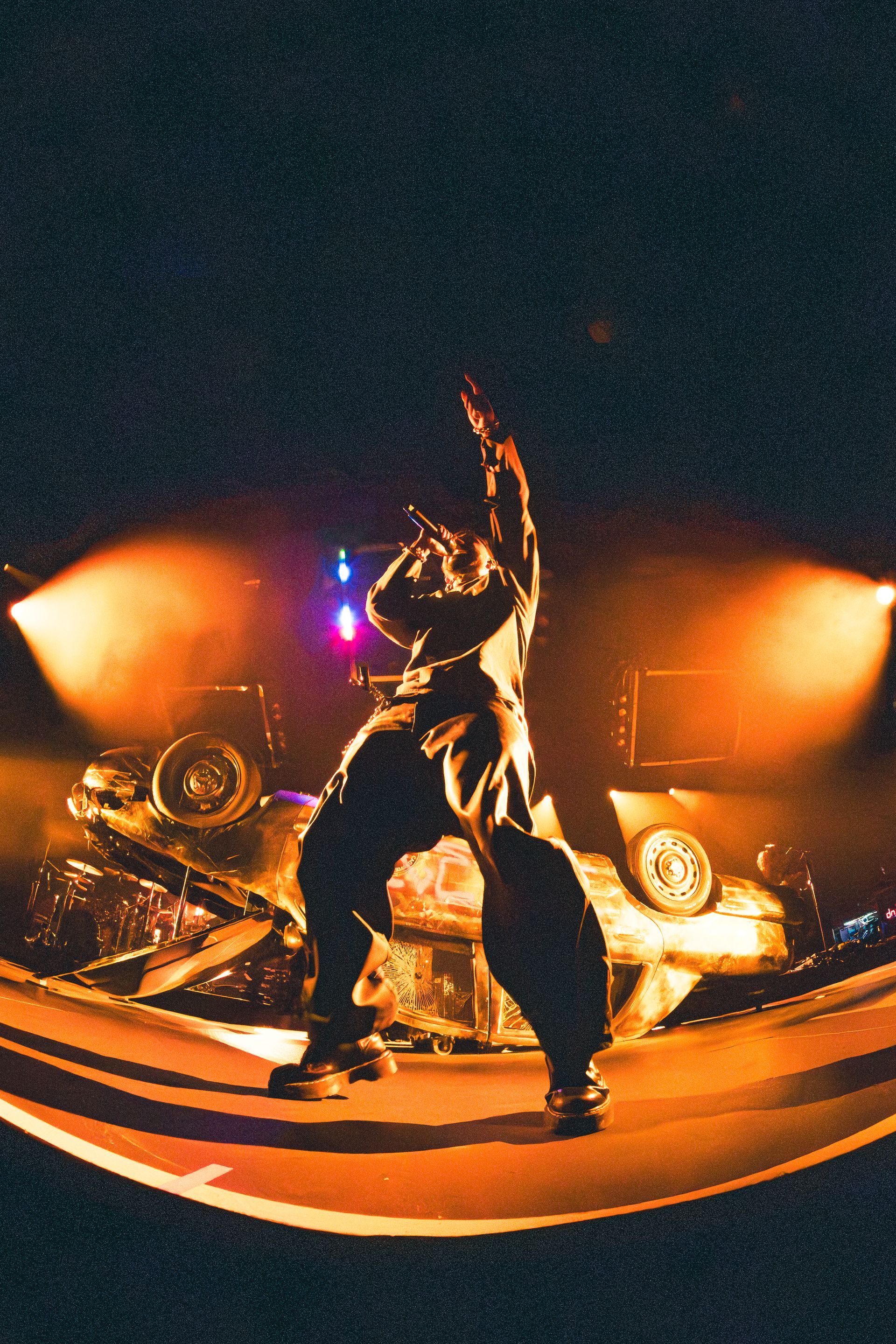Miguel performing on a stage under orange lights, surrounded by smoke and bright concert lighting