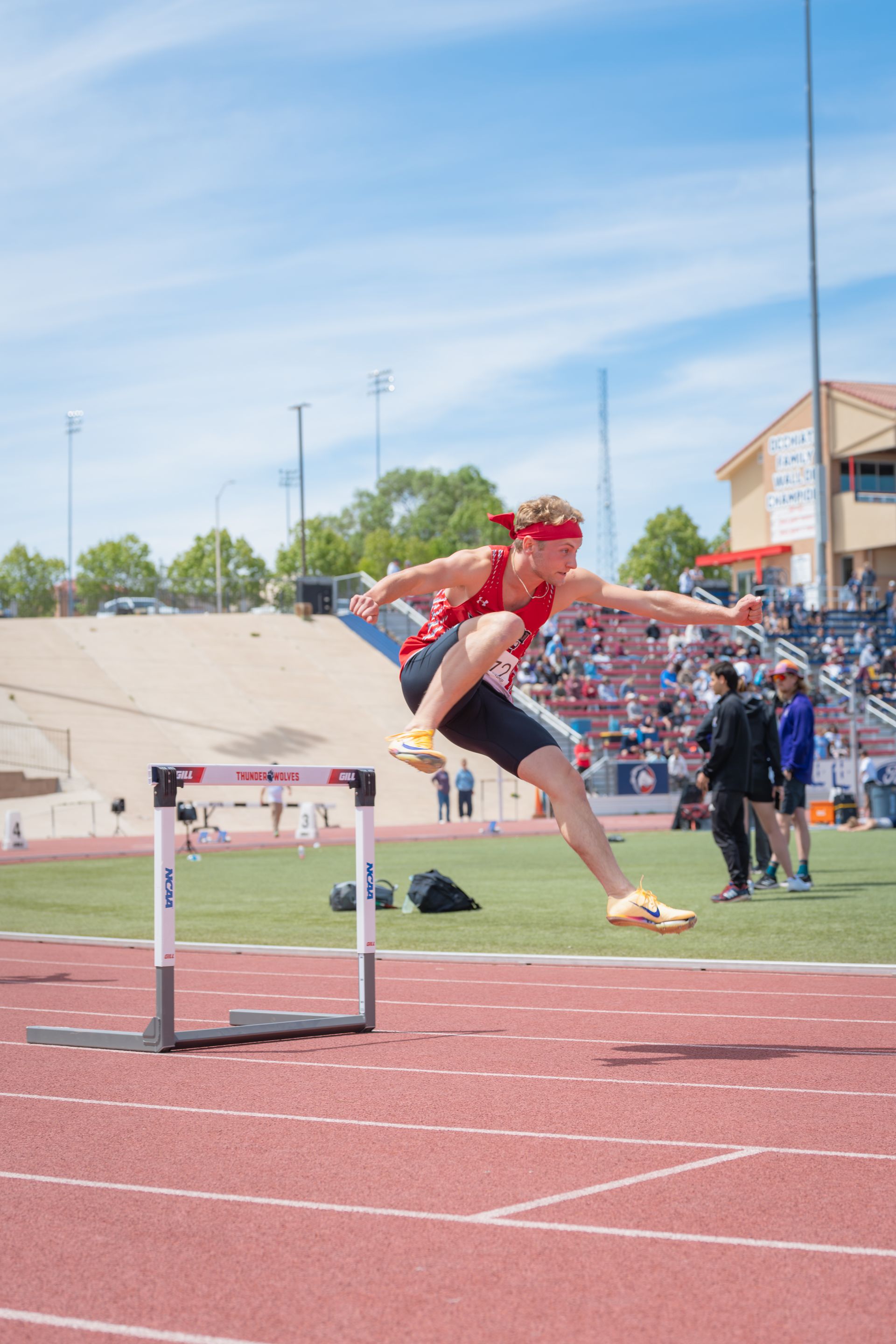 Athlete in red clears a hurdle on a track field during a race