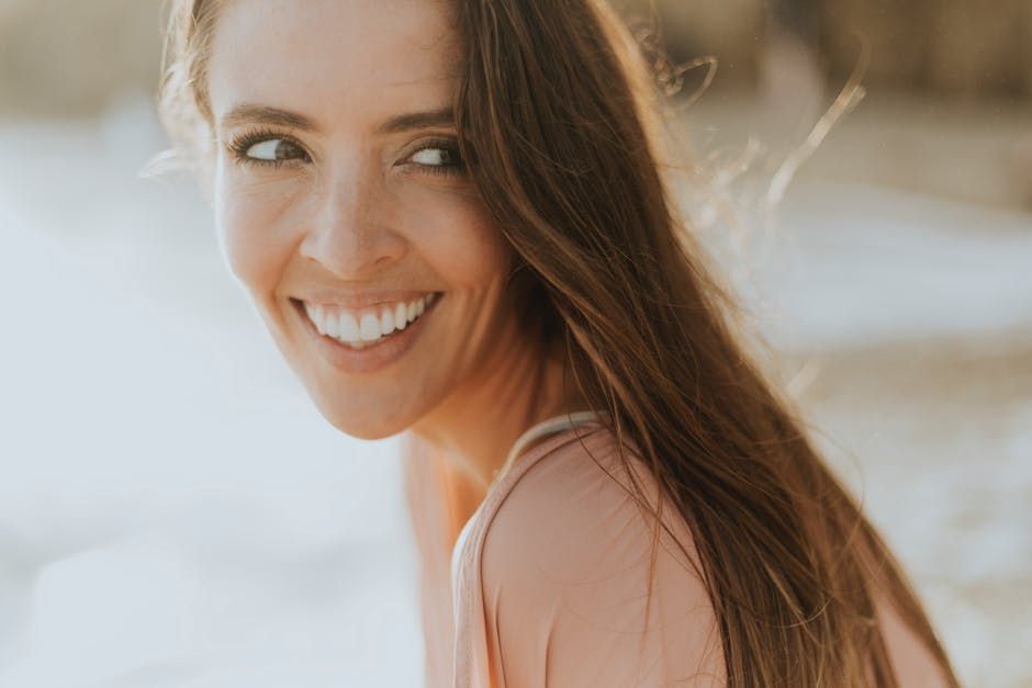 A woman with long hair is smiling and looking over her shoulder at the camera.