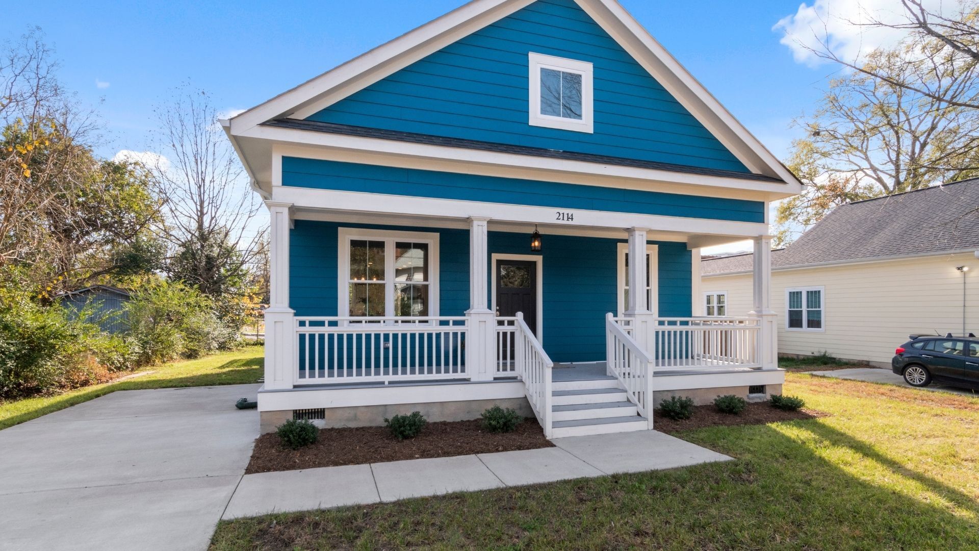 Blue house with white porch and trim; concrete driveway, grassy yard.