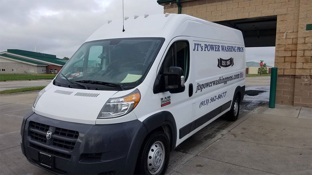 White Dodge Ram ProMaster van with business logo parked near a brick building.