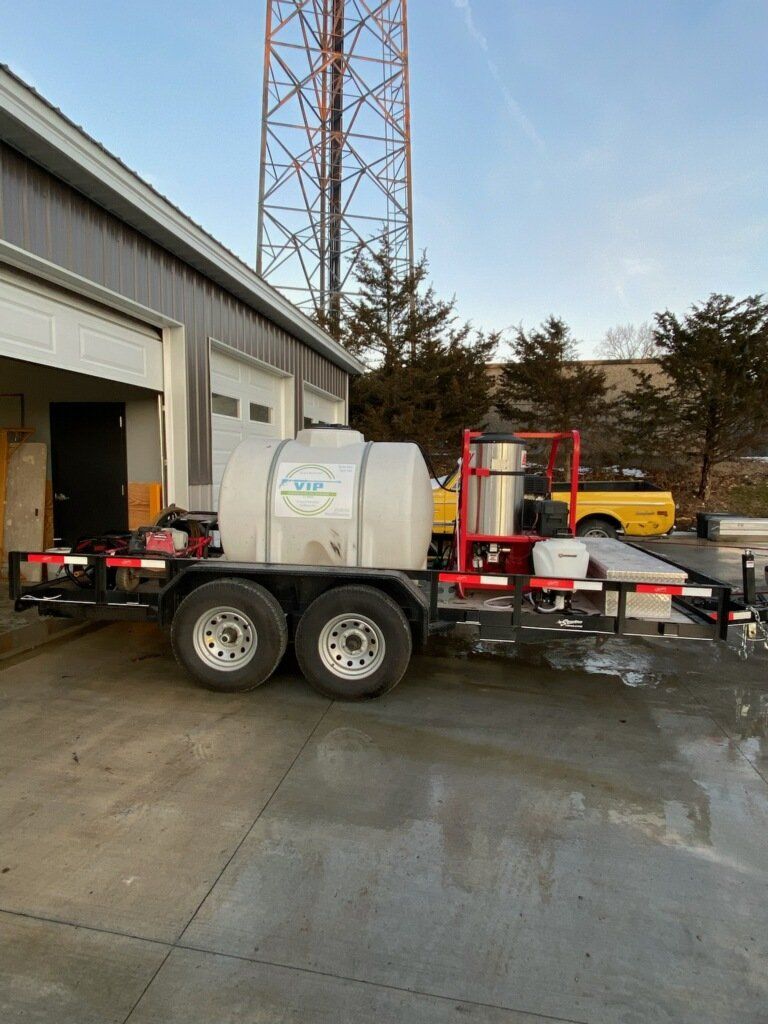 A trailer with a water tank and machinery parked outside a building, with a radio tower in the background.