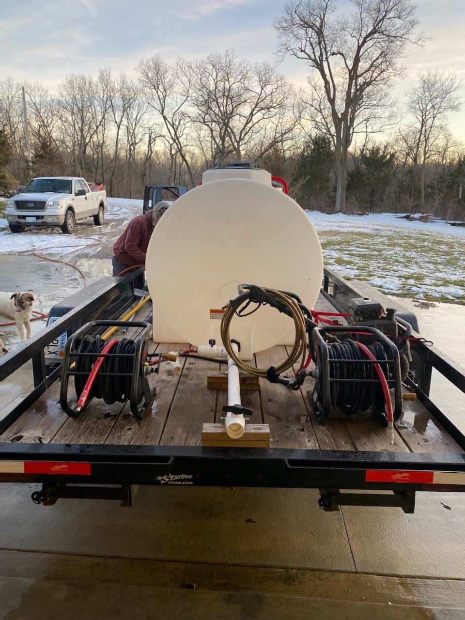 A trailer with a large white tank and two black generators. Person working on the equipment. Snow on the ground.