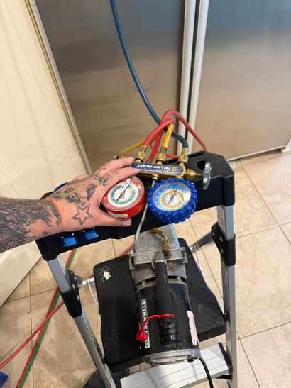 Hand testing HVAC manifold gauges on a refrigeration unit, with red, blue, and yellow hoses attached.