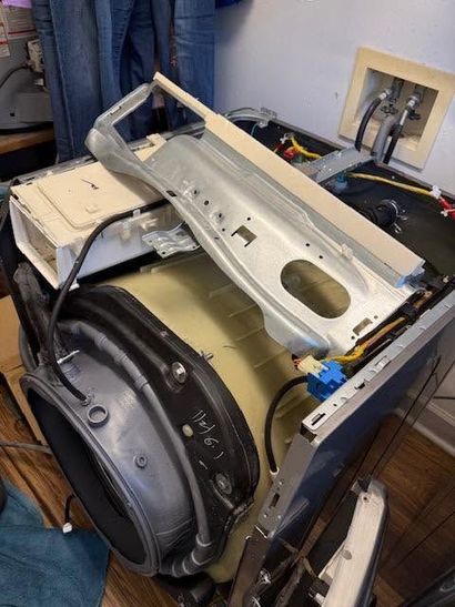 Disassembled car door and interior panel on a workbench in a garage, with tools and wiring visible