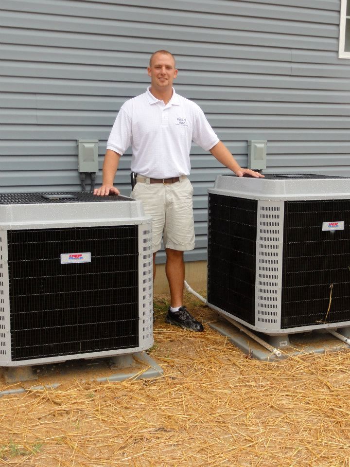 Man standing next to two air conditioning units outside a building.