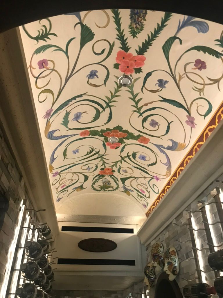 An arched ceiling painted with colorful floral vines and scrollwork, illuminated by recessed lighting above stone walls.
