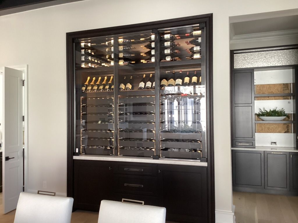 A dark wood, glass-enclosed wine display cabinet built into a white wall, with wine bottles on shelves and cabinets below.