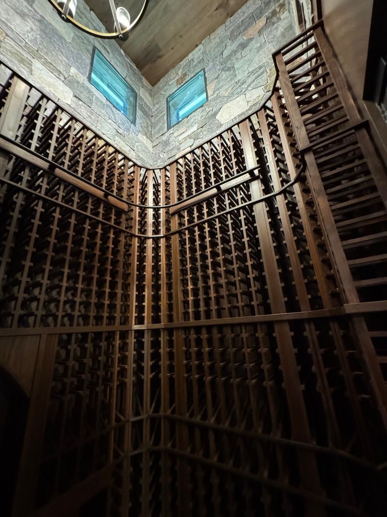 A high-angle view of a floor-to-ceiling wooden wine cellar with gridded storage racks and stone corner walls.
