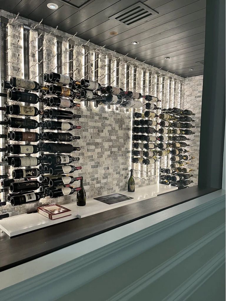 A modern wine display with wall-mounted racks holding bottles against a gray stone wall, over a white bar counter.