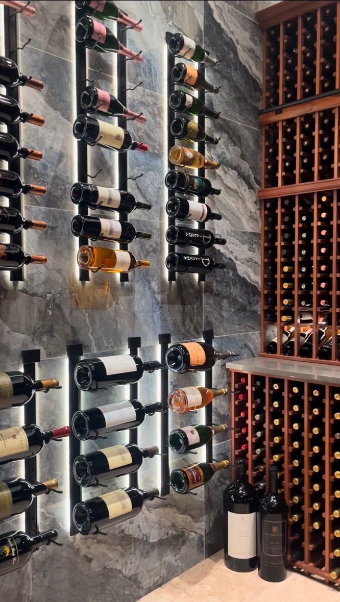 A wine cellar featuring backlit wall-mounted racks with bottles on a dark stone wall, next to traditional wooden racks.