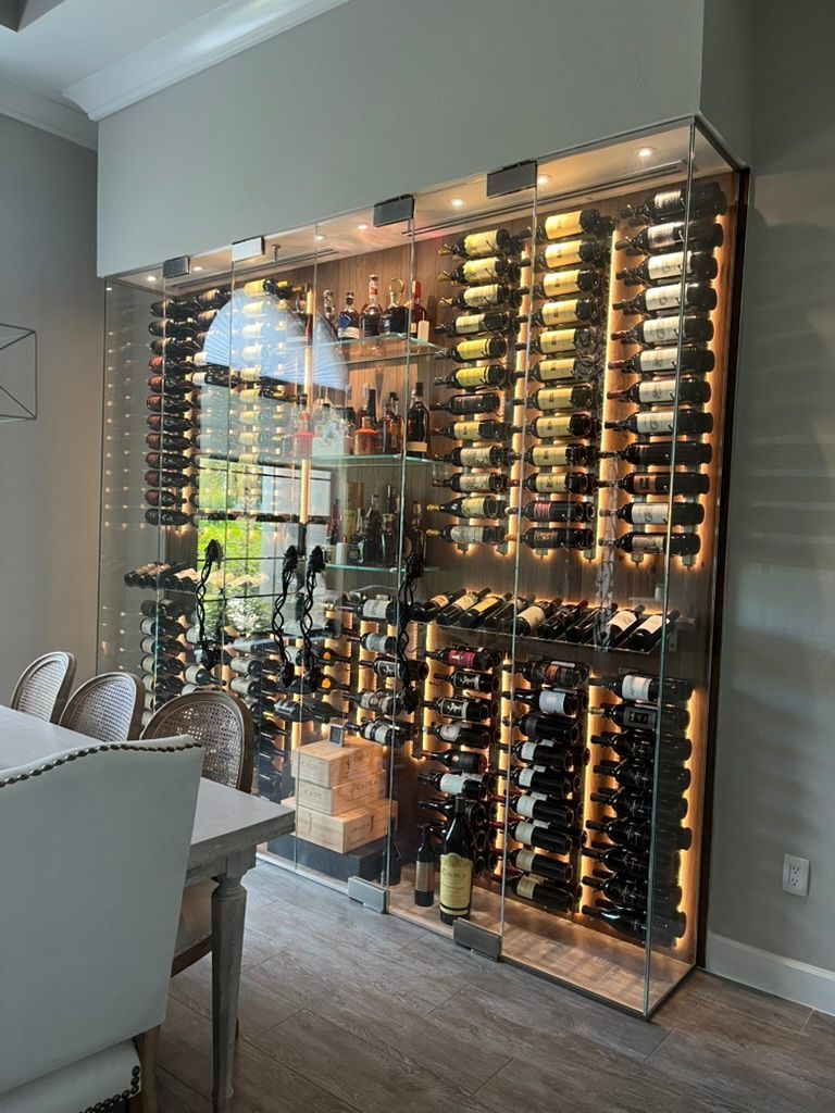 A large, glass-enclosed, illuminated wine rack filled with wine bottles in a dining room.