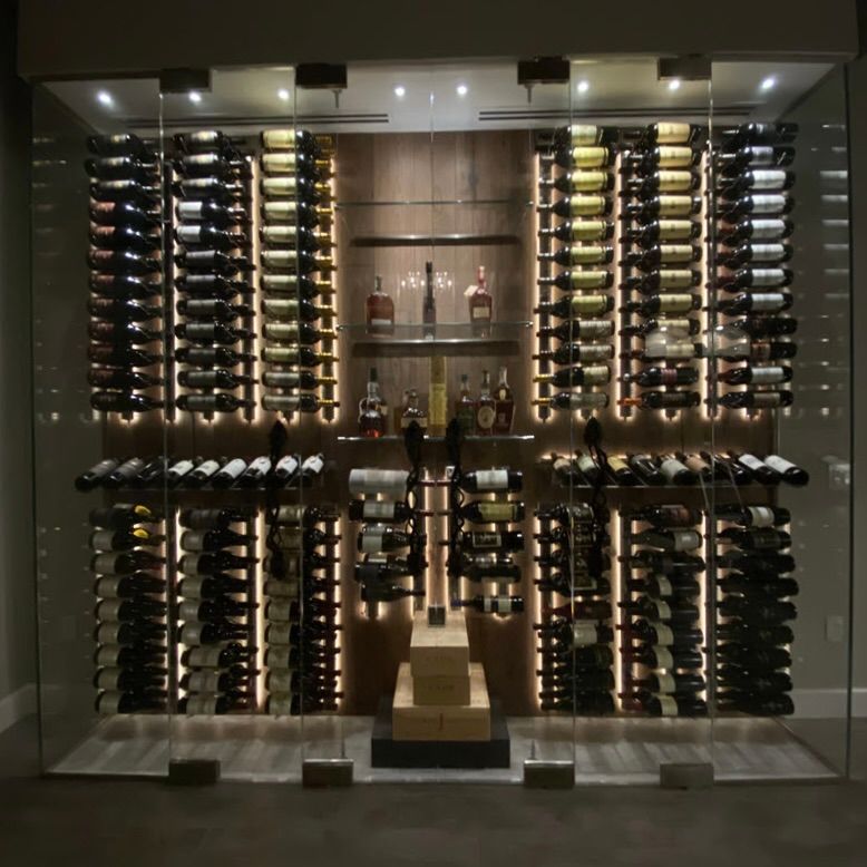 A modern, glass-enclosed wine cellar with illuminated racks displaying bottles in organized rows and shelves.