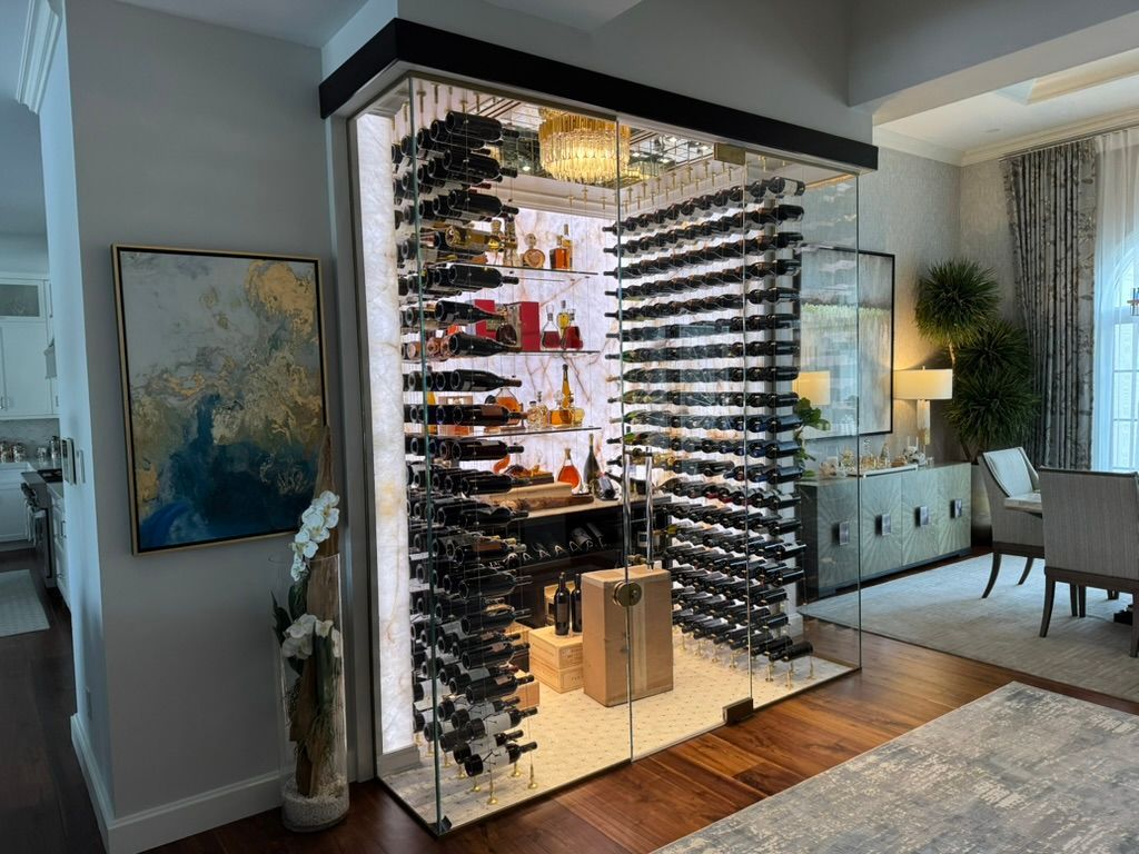 A modern, glass-enclosed wine cellar with illuminated shelving racks displaying wine bottles in a luxury home interior.