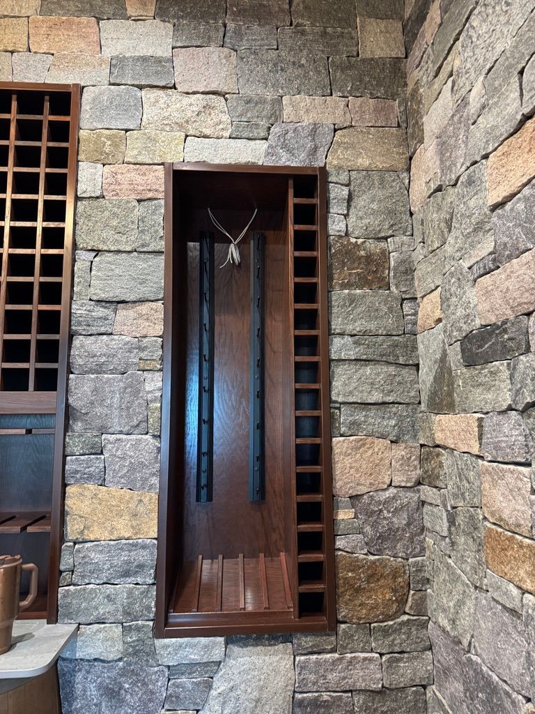 Built-in dark wood storage niche with vertical racks for wine bottles, set into a textured, rustic stone wall.