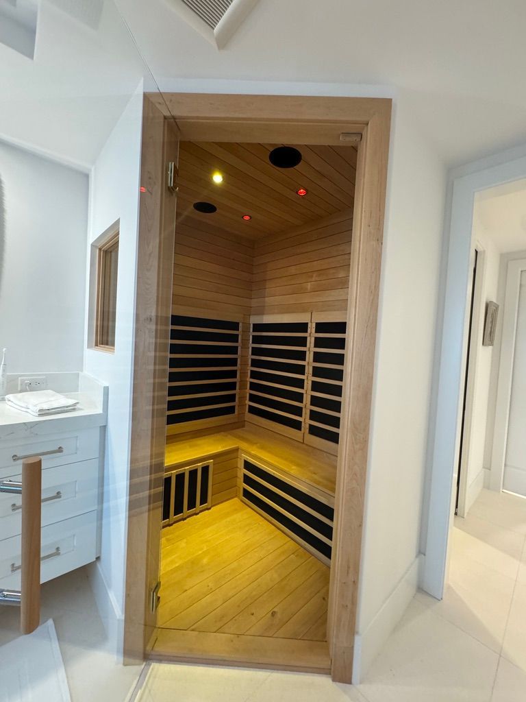 A wooden home sauna with L-shaped seating and black panel heaters inside a bright, modern room.