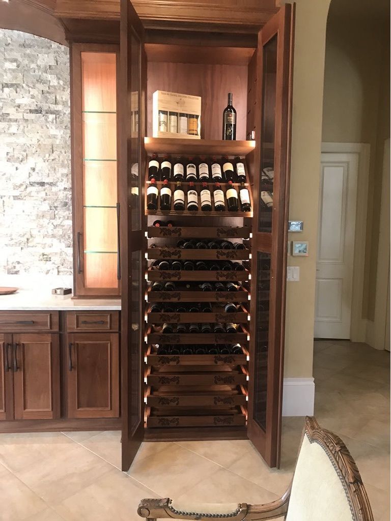 A tall wooden wine cabinet built into a wall, featuring glass doors and multiple rows of bottle racks in a home setting.