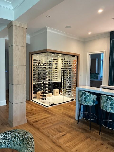 A custom, glass-enclosed wine cellar with interior lighting, wood floors, and bar seating in a modern home interior.