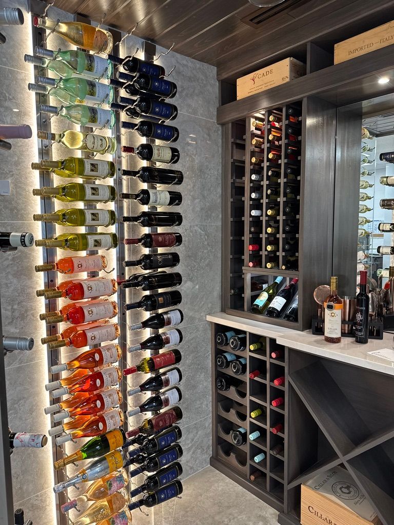A modern, illuminated wine cellar with rows of wall-mounted bottles and a wooden storage cabinet on the right.