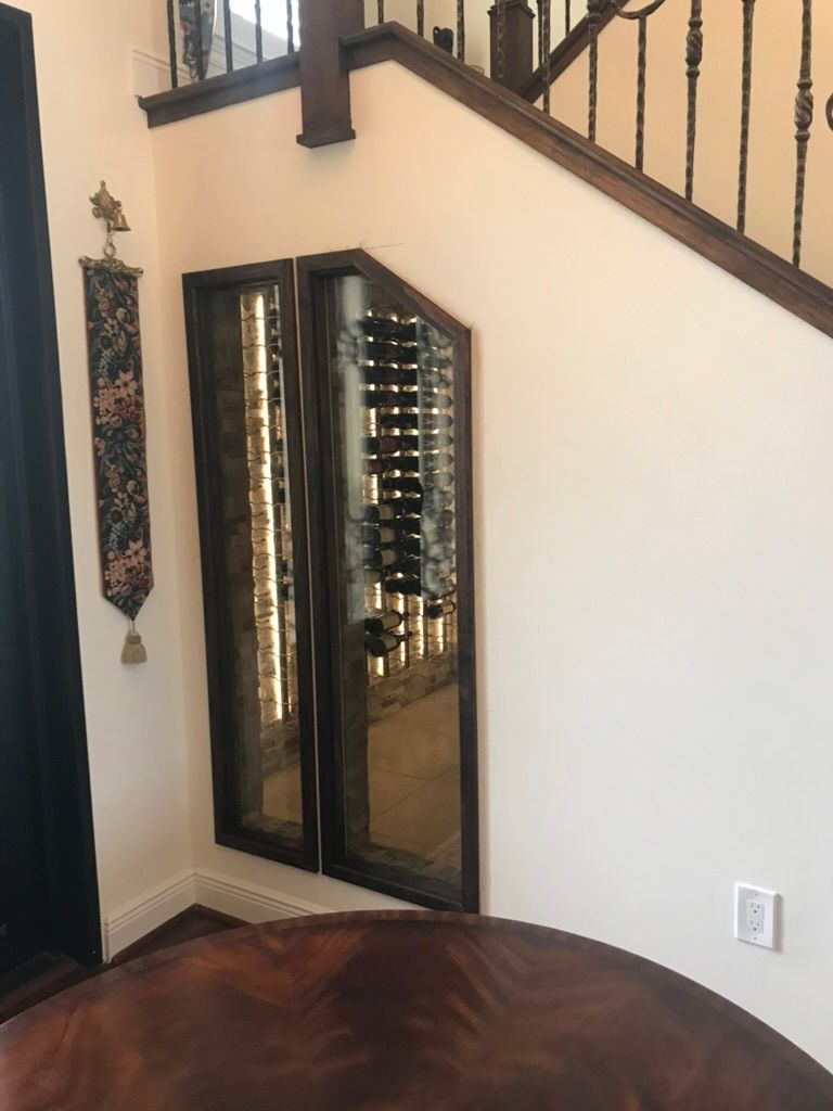 A custom wine rack built into the wall under a wooden staircase in a home.