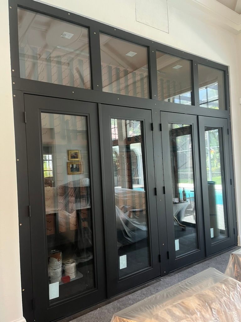 Black-framed four-panel glass patio doors with rectangular transom windows above, set into a white indoor wall.