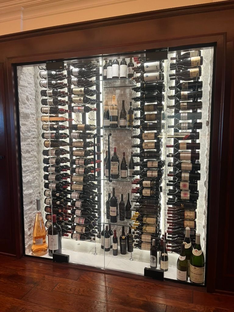 A large, illuminated wine cellar display featuring multiple rows of bottled wine in a dark wood frame.