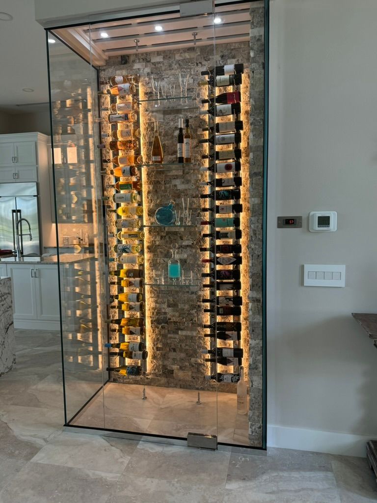 A modern, glass-enclosed wine display with two vertical racks mounted against a textured stone wall with LED lighting.