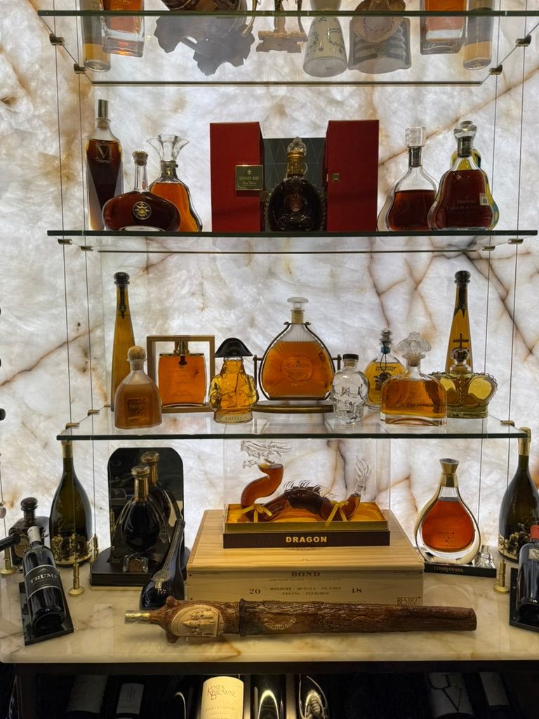 A brightly backlit display shelf holding various bottles of premium spirits, including Cognac and liqueurs.