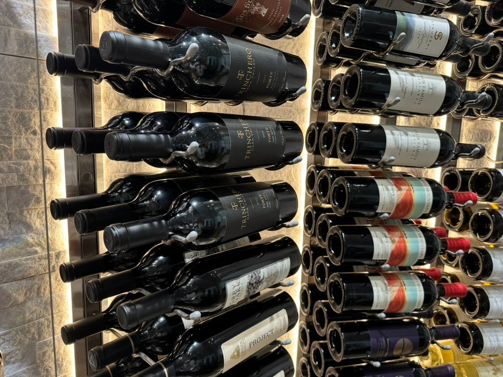 Two columns of wine bottles stored horizontally on a lit shelf.