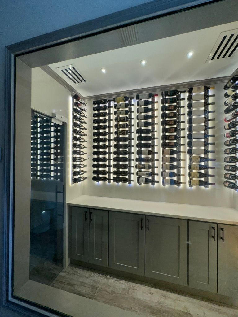 A modern wine cellar with backlit horizontal wine racks mounted above gray cabinets and a white countertop.