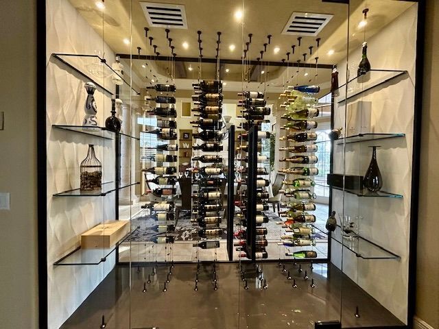 A modern glass wine cellar with floor-to-ceiling metal racks, wine bottles, and glass shelving on the sides.