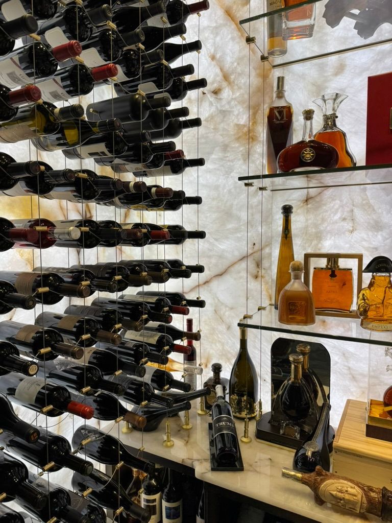 A wall of wine bottles stored on metal racks beside backlit display shelves featuring various glass liquor decanters.