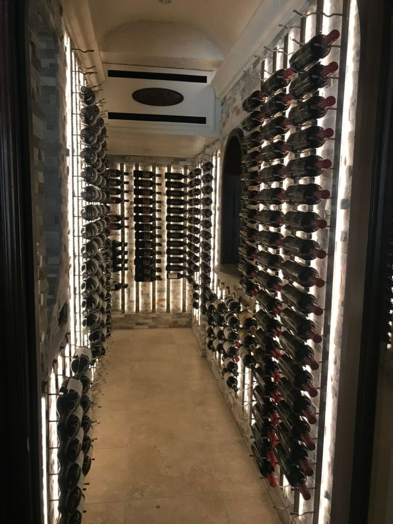 A narrow wine cellar with floor-to-ceiling metal bottle racks illuminated by vertical strips of light on both walls.