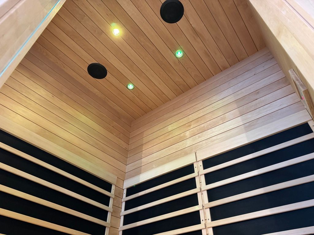 A sauna corner with light-colored wooden walls and ceiling, dark infrared panels, and small recessed ceiling lights.